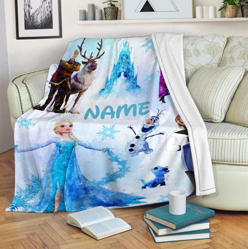 May include: A blue and white fleece blanket with a watercolor design featuring characters from the movie Frozen. The blanket features Elsa, Anna, Olaf, Kristoff, and Sven. The blanket also includes the text "NAME" in blue.