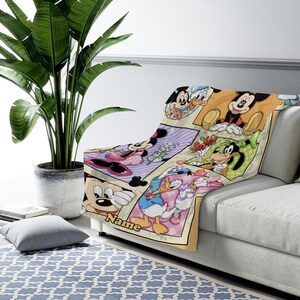 K&ouml;nnte beinhalten: Eine weiche Wohndecke mit einem farbenfrohen Raster aus Disney-Figuren, darunter Mickey Maus, Minnie Maus, Donald Duck, Daisy Duck und Goofy. Die Decke enth&auml;lt das Wort Name, das in gelber Schrift am unteren Rand des Designs gedruckt ist.