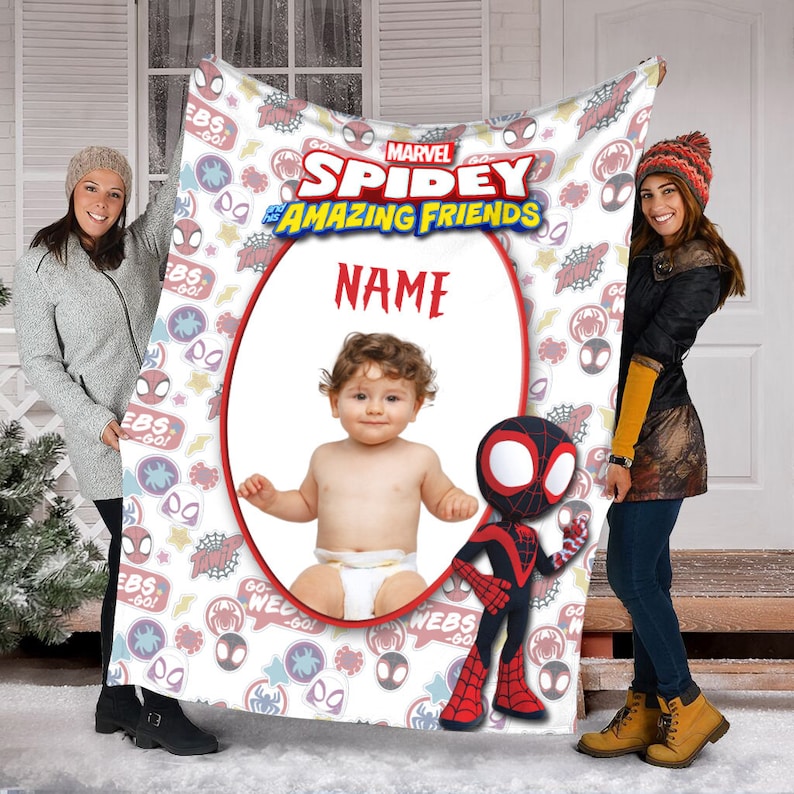 May include: A white fleece blanket featuring the Marvel Spidey and His Amazing Friends logo, a central oval frame with the text NAME above a baby in a diaper, and a graphic of a red and black spider character, surrounded by colorful icons.