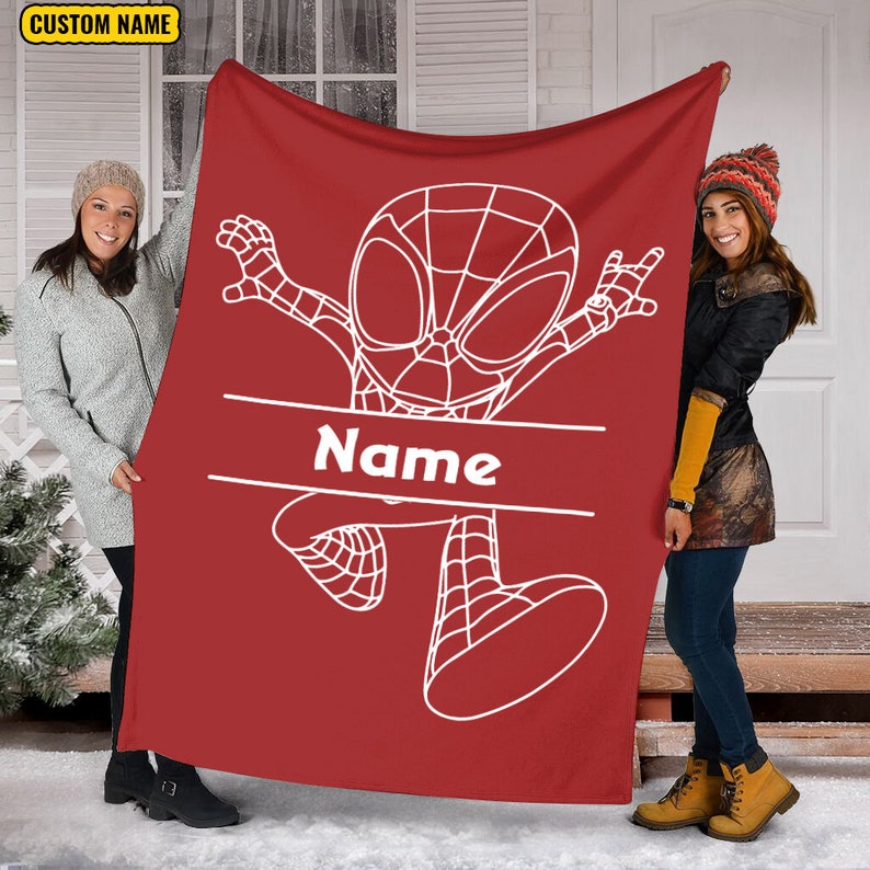 May include: A red fleece blanket featuring a white line art illustration of a cartoon superhero character in a dynamic pose. A horizontal white banner across the center contains the text Name in white letters. The blanket has a solid red background.