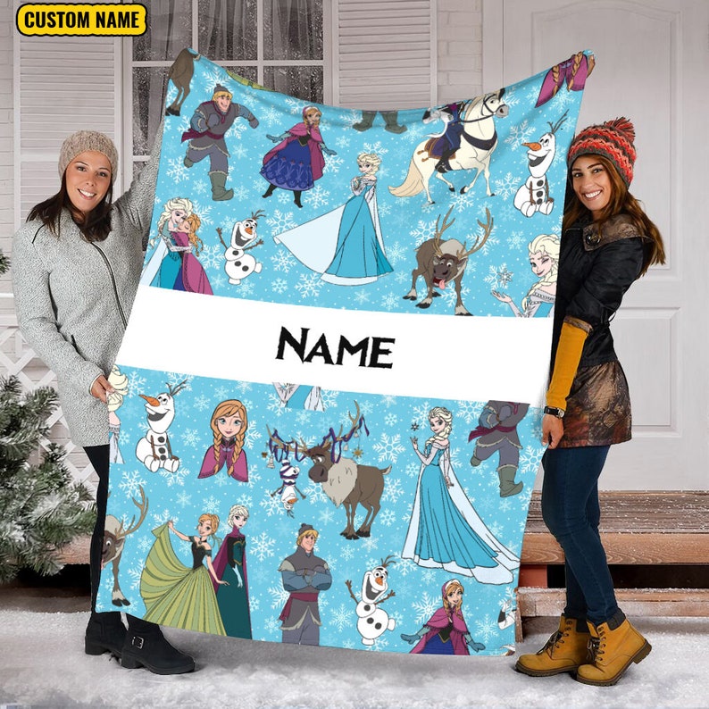 Pu&ograve; includere: Una coperta in pile azzurra con un motivo ripetuto di personaggi del film Frozen, tra cui Elsa, Anna, Olaf, Kristoff e Sven, con fiocchi di neve bianchi e una fascia orizzontale bianca centrale che riporta il testo NAME.