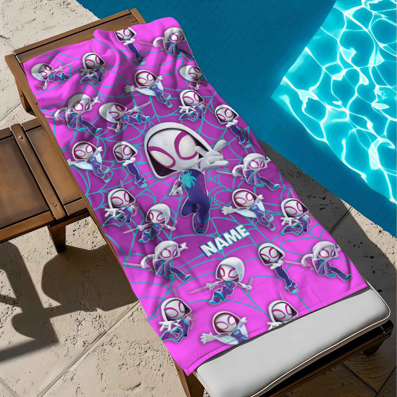 K&ouml;nnte beinhalten: Ein rechteckiges Strandtuch mit einem sich wiederholenden Muster einer Zeichentrickfigur in einem wei&szlig;en, violetten und rosafarbenen Kapuzenanzug vor einem rosa Hintergrund mit blauem Spinnennetzdesign. Eine gro&szlig;e Figur tr&auml;gt den Text NAME.