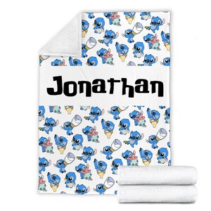 May include: A white fleece blanket featuring a repeating pattern of the blue character Stitch in various poses, including holding a baby bottle. A horizontal white band across the center displays the name Jonathan in bold black lettering.