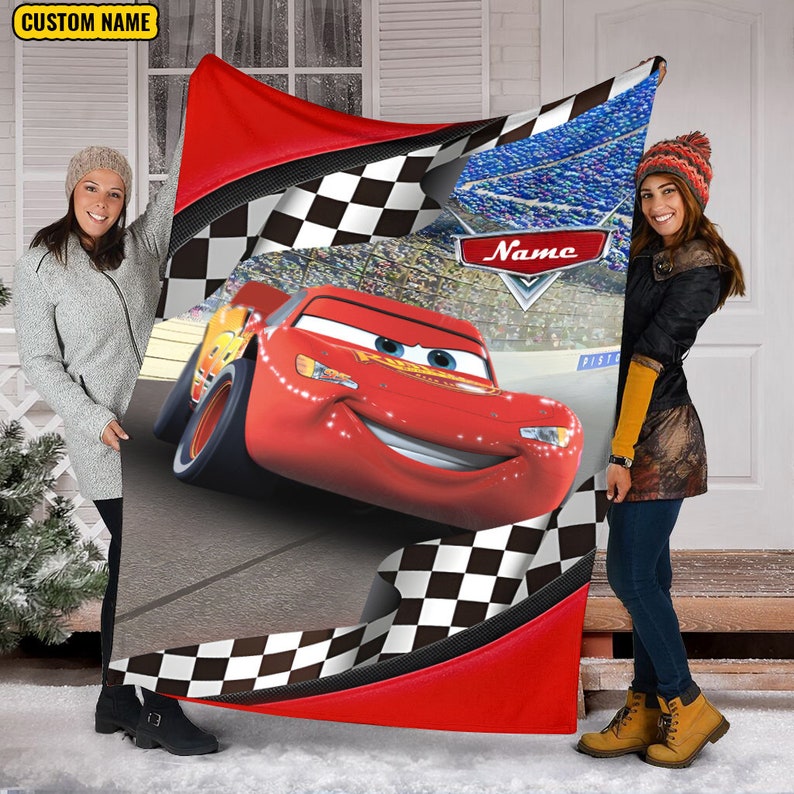 May include: A rectangular blanket featuring a red race car character with large eyes and a smile on a racetrack. The design includes a black and white checkered border, a stadium crowd background, and a red emblem with the text Name.