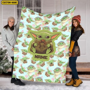 Może przedstawiać: Miękki, niebieski i zielony koc polarowy z powtarzającym się wzorem postaci z kresk&oacute;wek. Postać jest zielona z dużymi oczami i nosi brązowy płaszcz. Koc ma nadrukowany tekst "NAME".