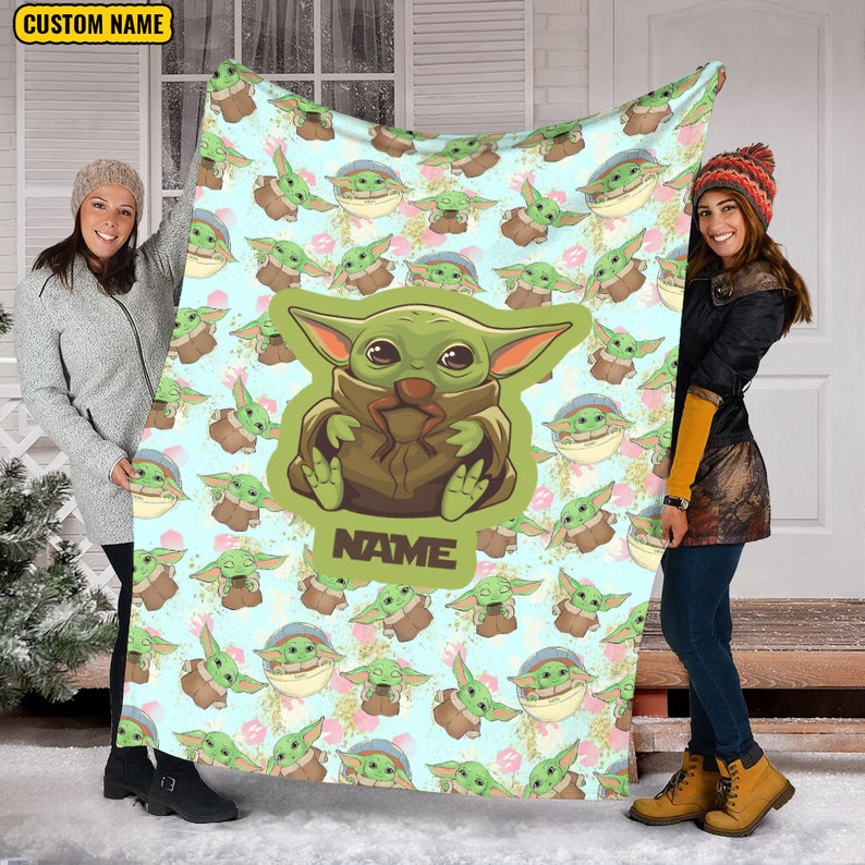 Może przedstawiać: Miękki, niebieski i zielony koc polarowy z powtarzającym się wzorem postaci z kresk&oacute;wek. Postać jest zielona z dużymi oczami i nosi brązowy płaszcz. Koc ma nadrukowany tekst "NAME".