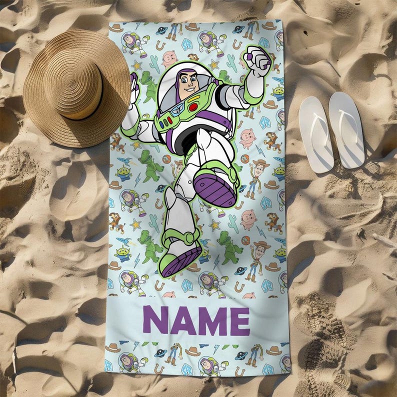 May include: A rectangular beach towel featuring a repeating pattern of Toy Story characters including Buzz Lightyear, Woody, and Rex on a light blue background. A large Buzz Lightyear graphic is centered, and the word NAME is printed in purple.