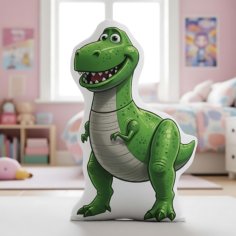May include: A green cartoon Tyrannosaurus Rex pillow with a smiling expression. The dinosaur has a light gray belly and a white outline. The pillow is on a white surface in a child's bedroom.