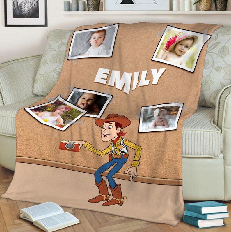 May include: A brown and tan fleece blanket with a corkboard design. The blanket features a cartoon image of Woody from Toy Story holding a camera. There are several photos of babies on the blanket, along with the name "EMILY".