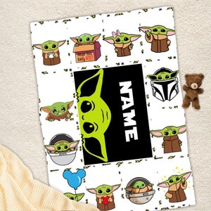 May include: A white blanket featuring a repeating pattern of green cartoon characters with large ears and brown robes. A large black rectangular center panel displays a green character silhouette and the white text NAME in capital letters.