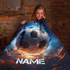 May include: A personalized fleece blanket with a fiery soccer ball design. The blanket features a soccer ball engulfed in flames and the word "NAME" in a distressed white font.