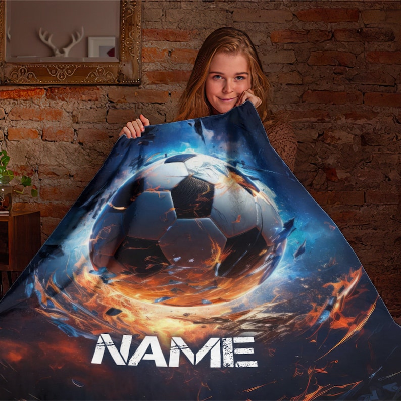 May include: A personalized fleece blanket with a fiery soccer ball design. The blanket features a soccer ball engulfed in flames and the word "NAME" in a distressed white font.