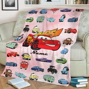 Puede incluir: Manta de forro polar rosa con tem&aacute;tica de Cars. La manta presenta a Rayo McQueen, Mate y otros personajes de la pel&iacute;cula Cars de Disney Pixar. La manta est&aacute; personalizada con el nombre "Name".