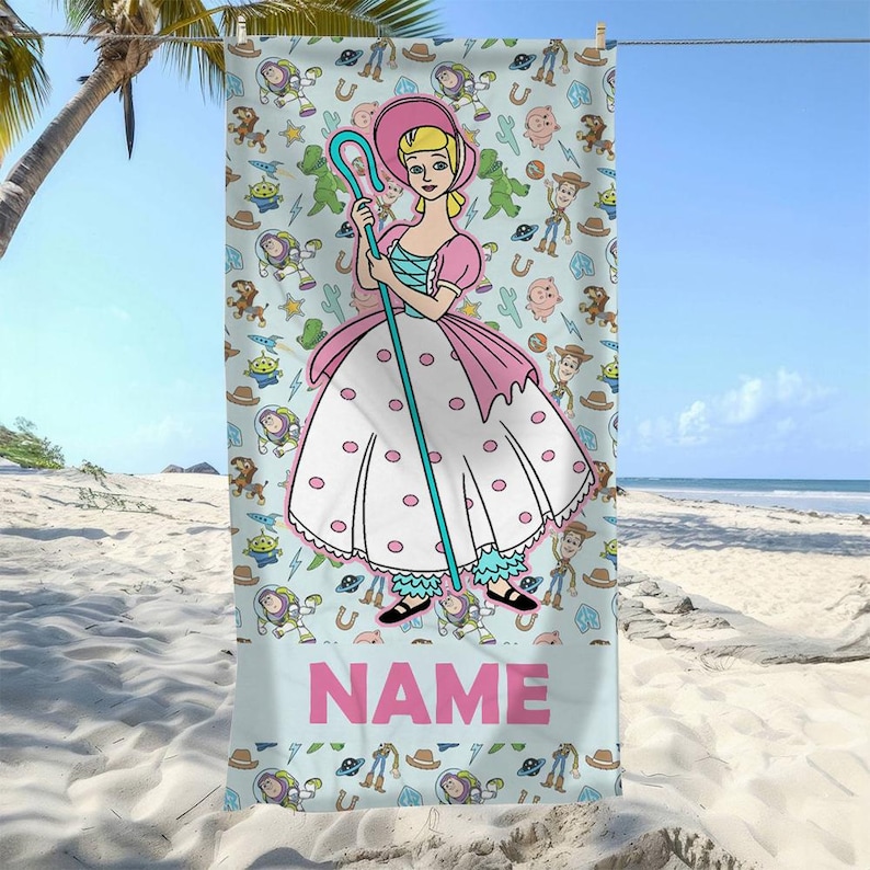 May include: A light blue beach towel featuring a central illustration of Bo Peep holding a blue shepherd's crook, surrounded by a repeating pattern of Toy Story characters including Buzz Lightyear and Woody. The word NAME is printed in pink.