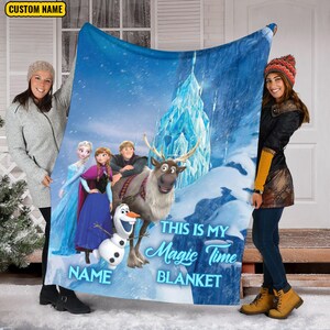 May include: A rectangular fleece blanket featuring a blue winter scene with Elsa, Anna, Kristoff, Sven, and Olaf. The text reads "THIS IS MY MAGIC TIME BLANKET" and includes a placeholder for a custom name. The background shows an ice castle.