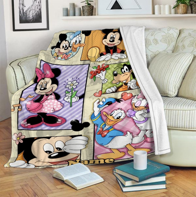 K&ouml;nnte beinhalten: Eine Pl&uuml;schdecke mit einem mehrteiligen Grafikdruck von Disney-Figuren wie Mickey Maus, Minnie Maus, Donald Duck, Daisy Duck und Goofy. Das Design umfasst eine wei&szlig;e Fleece-Unterseite und das Wort Name, das unten aufgedruckt ist.