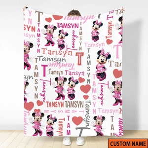 May include: A white fleece blanket featuring a repeating pattern of Minnie Mouse in a pink polka dot dress, red hearts, and the name Tamsyn printed in various pink, brown, and grey fonts. The design includes vertical and horizontal text layouts.