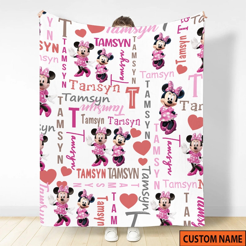 May include: A white fleece blanket featuring a repeating pattern of Minnie Mouse in a pink polka dot dress, red hearts, and the name Tamsyn printed in various pink, brown, and grey fonts. The design includes vertical and horizontal text layouts.