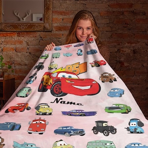 Puede incluir: Una manta de forro polar rosa con tem&aacute;tica de Cars. La manta presenta una variedad de personajes de Cars, incluyendo Rayo McQueen, Mate y los otros coches de la pel&iacute;cula. La manta est&aacute; personalizada con el nombre "Name".