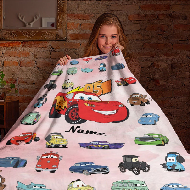 Puede incluir: Una manta de forro polar rosa con tem&aacute;tica de Cars. La manta presenta una variedad de personajes de Cars, incluyendo Rayo McQueen, Mate y los otros coches de la pel&iacute;cula. La manta est&aacute; personalizada con el nombre "Name".