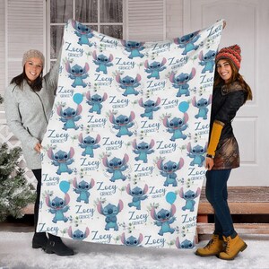 May include: A white fleece blanket featuring a repeating pattern of the blue character Stitch from Lilo and Stitch, interspersed with blue balloons and the personalized text Zoey Grace in a cursive blue font across the entire fabric surface.