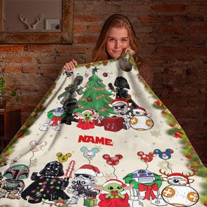 Puede incluir: Una manta de forro polar blanca con un &aacute;rbol de Navidad y personajes de Star Wars. Los personajes est&aacute;n vestidos con atuendos festivos y sostienen regalos. La manta est&aacute; personalizada con la palabra "NAME".