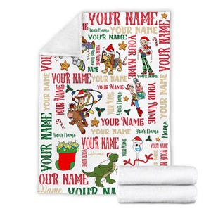 May include: A white fleece blanket with a repeating pattern of Toy Story characters wearing Santa hats and Christmas lights. The text "YOUR NAME" is repeated throughout the pattern.
