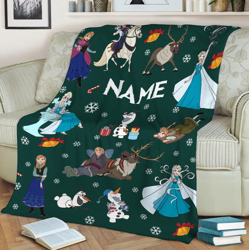 May include: A dark green throw blanket featuring a repeating pattern of Frozen characters including Elsa, Anna, Olaf, Kristoff, and Sven, interspersed with white snowflakes, red candy canes, and yellow bells, with the word NAME printed in white.