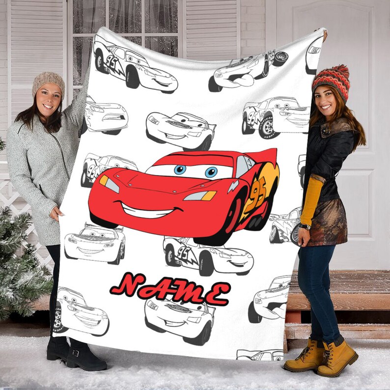 May include: A white fleece blanket featuring a large, colorful illustration of the red race car Lightning McQueen from the movie Cars, surrounded by multiple black and white line art sketches of the same character, with the red text NAME below.