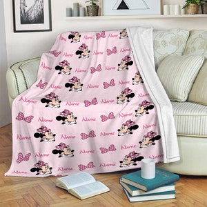 May include: Pink fleece blanket with a repeating pattern of a cartoon character with a pink bow and the word "NAME" printed throughout.
