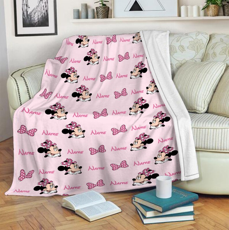 May include: Pink fleece blanket with a repeating pattern of a cartoon character with a pink bow and the word "NAME" printed throughout.