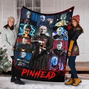 May include: A black blanket featuring a collage of images of Pinhead from the Hellraiser film series. The word "PINHEAD" is printed in red across the bottom. The blanket is held up by two people.
