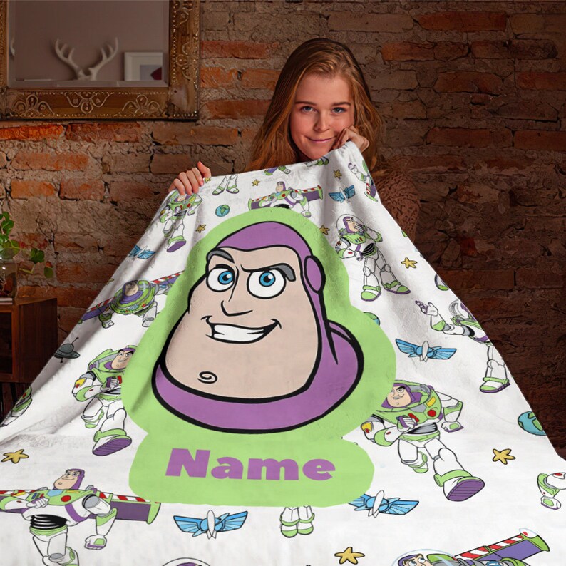 May include: A white fleece blanket featuring a repeating pattern of Buzz Lightyear characters in various poses. A large, central light green graphic displays a cartoon portrait of Buzz Lightyear's head and the purple text Name below it.