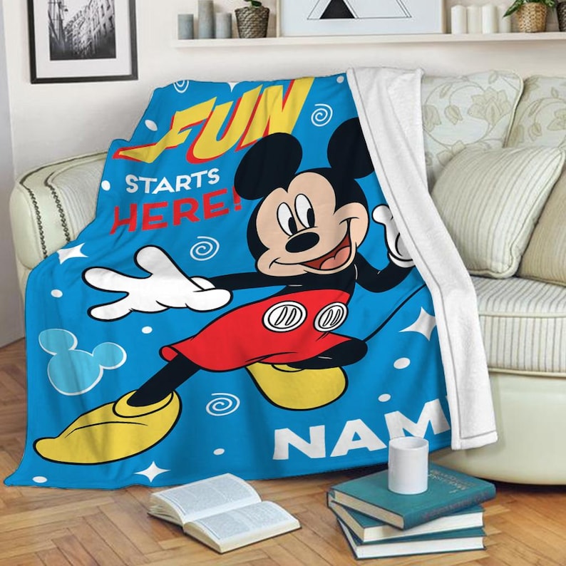 May include: Blue fleece blanket with a cartoon image of Mickey Mouse. The text "Fun Starts Here!" is printed on the blanket. The blanket is personalized with the name "NAM".