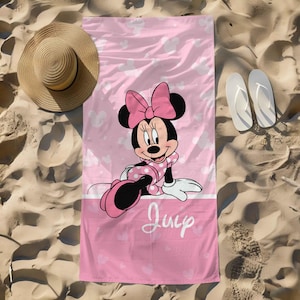 Puede incluir: Una toalla de playa rectangular con fondo rosa y siluetas blancas de Minnie Mouse, una ilustraci&oacute;n central de Minnie Mouse con vestido de lunares y lazo rosa, y el texto en cursiva blanca "July" en la parte inferior.