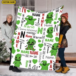 May include: A white fleece blanket with a repeating pattern of green and black cartoon characters. The characters are stitched together with red thread. The blanket has the words "Name" and "Name Name" repeated throughout the pattern.