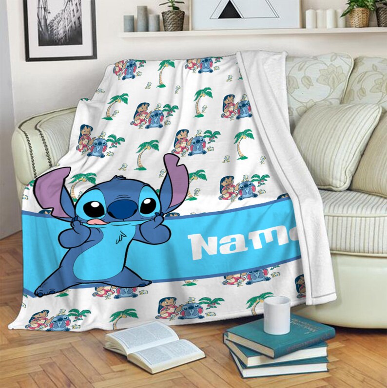 K&ouml;nnte beinhalten: Eine wei&szlig;e Fleecedecke mit einem sich wiederholenden Muster aus Stitch und Lilo mit Palmen. Ein breites blaues horizontales Band in der Mitte zeigt die Figur Stitch mit herausgestreckter Zunge und den teilweisen wei&szlig;en Text Name rechts.