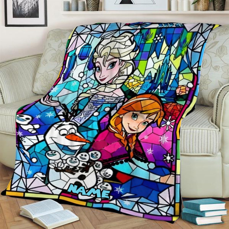 Pode incluir: Uma manta de fleece retangular com uma estampa colorida estilo vitral de Elsa, Anna e Olaf de Frozen. O design inclui padr&otilde;es geom&eacute;tricos em tons de azul, rosa e verde, com a palavra NAME impressa em letras azul-claras.