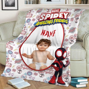 May include: A white fleece blanket featuring the Marvel Spidey and His Amazing Friends logo, a central oval frame for a custom photo, the word NAME in red text, and a repeating pattern of spider-themed icons, webs, and stars with a Spidey character.