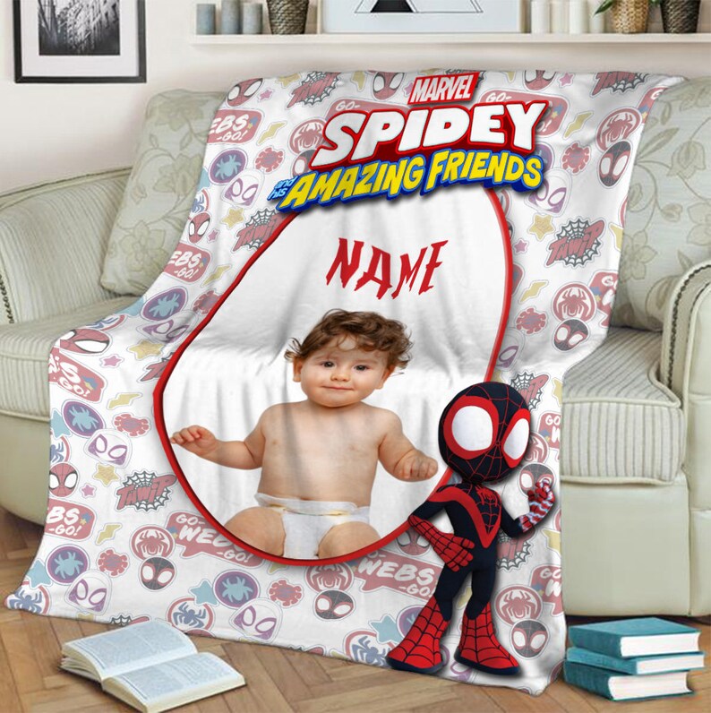 May include: A white fleece blanket featuring the Marvel Spidey and His Amazing Friends logo, a central oval frame for a custom photo, the word NAME in red text, and a repeating pattern of spider-themed icons, webs, and stars with a Spidey character.