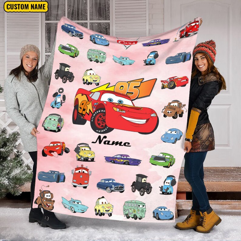Puede incluir: Una manta de forro polar rosa con tem&aacute;tica de Cars. La manta presenta a Rayo McQueen, Mate y otros personajes de Cars. La manta est&aacute; personalizada con el nombre "Name" y el n&uacute;mero "95".