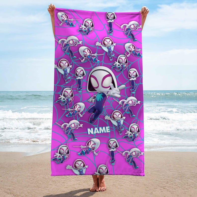 K&ouml;nnte beinhalten: Ein rechteckiges Strandtuch in leuchtendem Pink mit einem sich wiederholenden Muster aus Ghost-Spider-Figuren in verschiedenen Action-Posen vor einem hellblauen Spinnennetz-Hintergrund. Das Wort NAME ist in wei&szlig;en Blockbuchstaben mittig aufgedruckt.