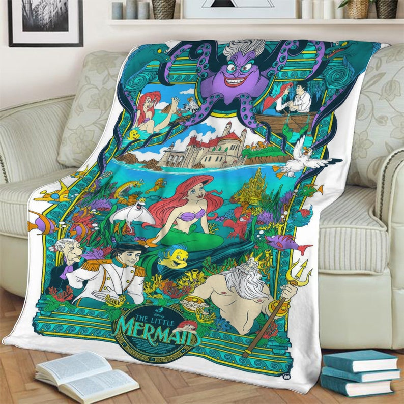 May include: A white fleece blanket featuring a colorful graphic print of The Little Mermaid characters including Ariel, King Triton, Prince Eric, and Ursula. The design includes underwater scenes, a castle, and the text The Little Mermaid.