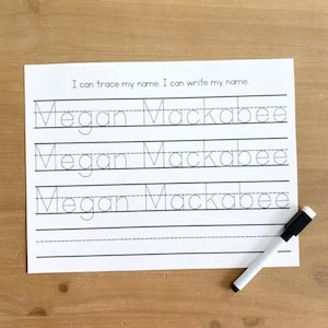 May include: A white paper with the text "I can trace my name. I can write my name." and the name "Megan Mackabee" printed three times in dotted lines for tracing. A black and white dry-erase marker rests on the paper.