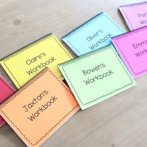 Large kindergarten workbook with laminated pages. Books are laid out to show the variety of colors. Each book is personalized with a different childs name