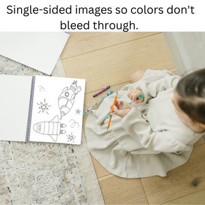 May include: A child sits on a wooden floor, coloring in a book with a rocket ship illustration. The book has a spiral binding and single-sided pages. The text "Single-sided images so colors don't bleed through." is at the top of the image.