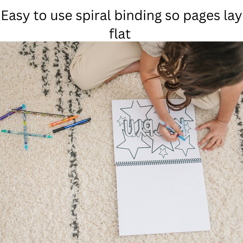 May include: A child sits on a rug and colors in a spiral bound coloring book with a blue marker. The book has a black and white illustration of stars and the word "WAK" inside the stars. The book is open to a blank page. There are several colored pens and pencils on the rug.