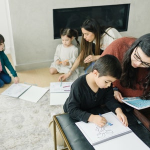 May include: A group of children are coloring in a book. One child is sitting on a bench and coloring a picture of a crab. The other children are sitting on the floor and coloring in their own books.