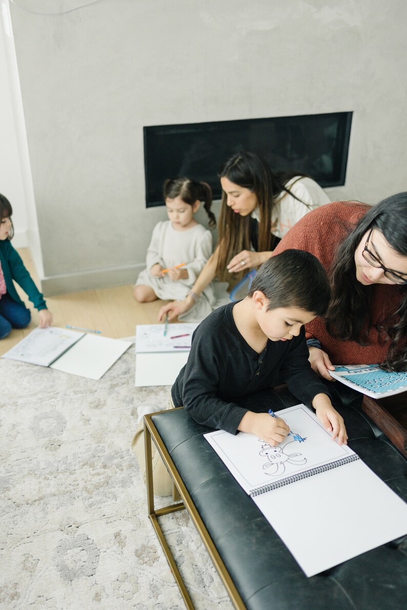 May include: A group of children are coloring in a book. One child is sitting on a bench and coloring a picture of a crab. The other children are sitting on the floor and coloring in their own books.