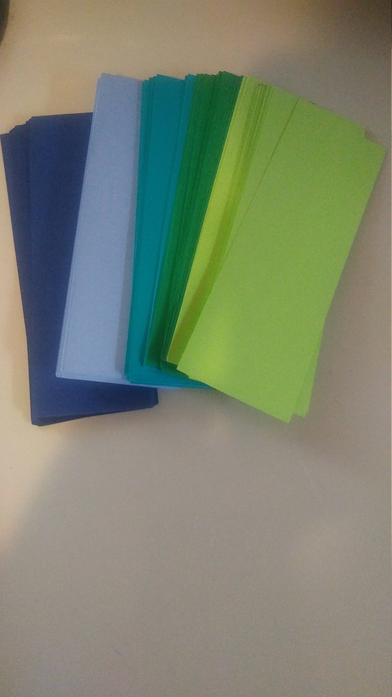 K&ouml;nnte beinhalten: Eine Sammlung farbiger Papierb&ouml;gen in Blau-, T&uuml;rkis-, Gr&uuml;n- und Limettengr&uuml;nt&ouml;nen. Die Bl&auml;tter sind gestapelt und aufgef&auml;chert, wodurch die Farbvielfalt zur Geltung kommt. Das Papier scheint rechteckig und von Standardgr&ouml;&szlig;e zu sein.